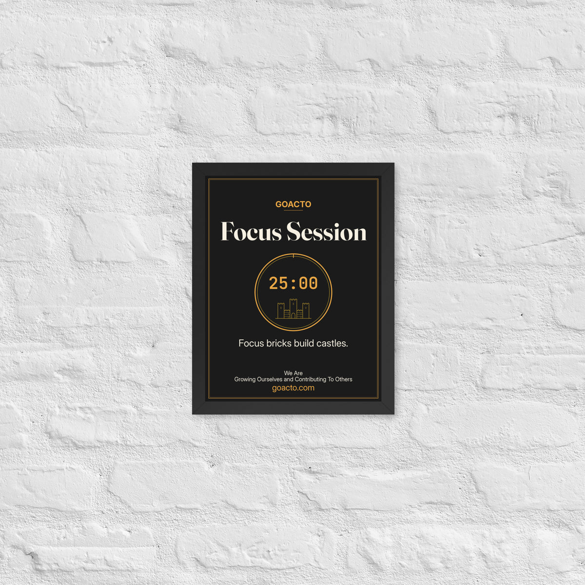 Focus Session Framed Print, Brick Rise design, 11x14 in a black frame on a white brick wall: thin amber ring around a 25:00 timer with a small line-drawn castle inside, on charcoal, the line 'Focus bricks build castles.' and 'We Are / Growing Ourselves and Contributing To Others' above goacto.com