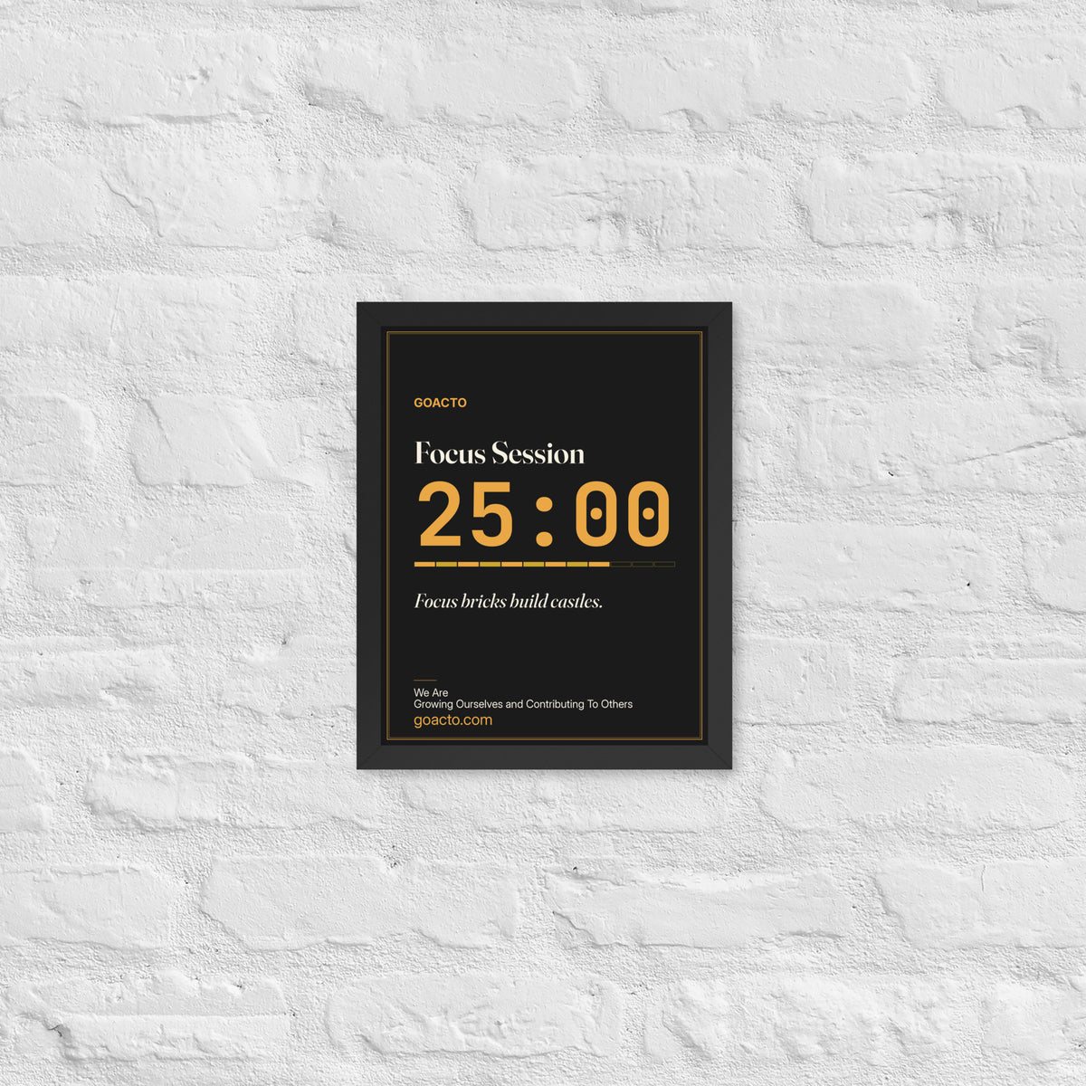 Focus Session Framed Print, Type design, 11x14 in a black frame on a white brick wall: oversized amber 25:00 above a segmented progress bar, on charcoal, the line 'Focus bricks build castles.' and 'We Are / Growing Ourselves and Contributing To Others' above goacto.com
