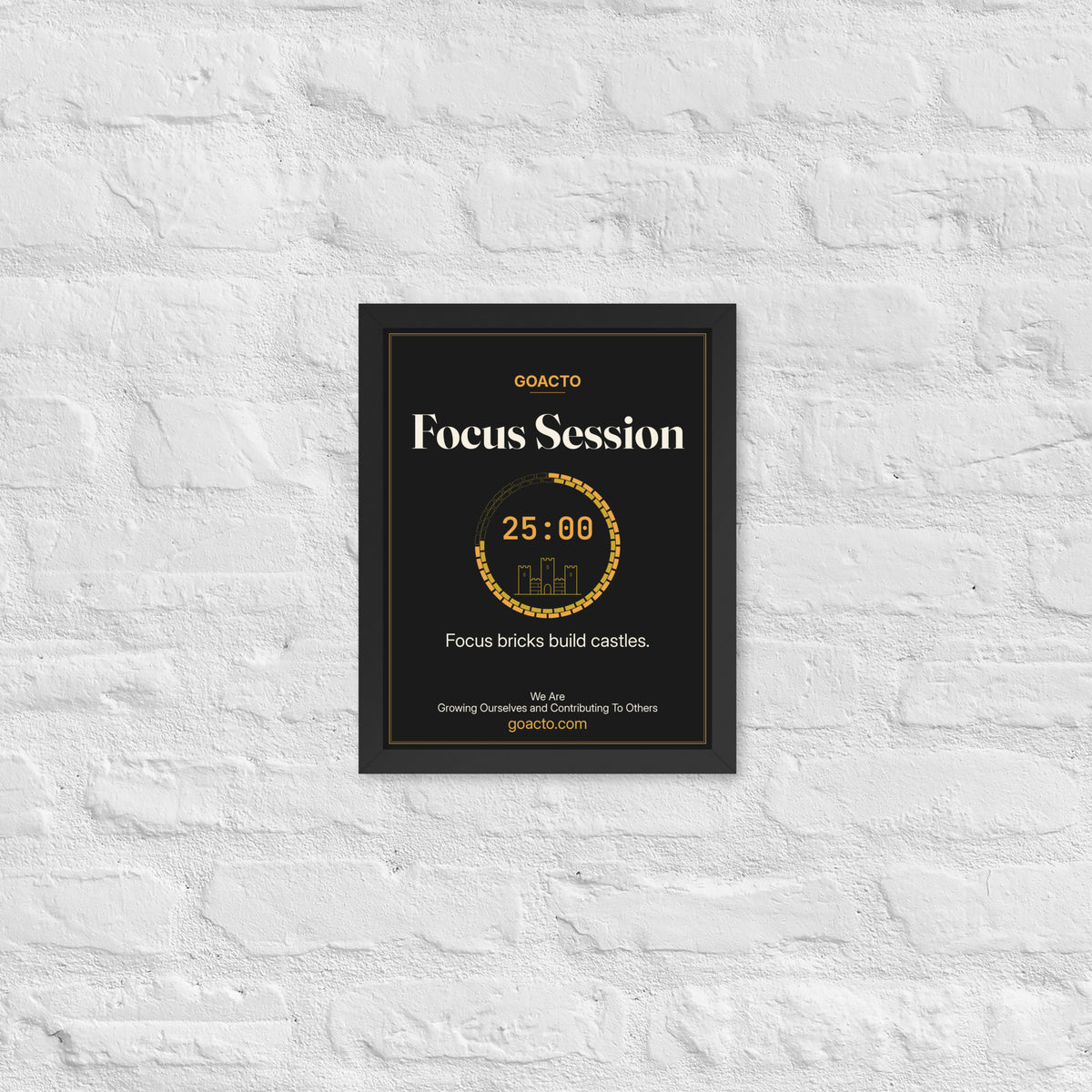 Focus Session Framed Print, Castle Ring design, 11x14 in a black frame on a white brick wall: ring of amber bricks around a 25:00 timer with a small line-drawn castle inside, on charcoal, the line 'Focus bricks build castles.' and 'We Are / Growing Ourselves and Contributing To Others' above goacto.com