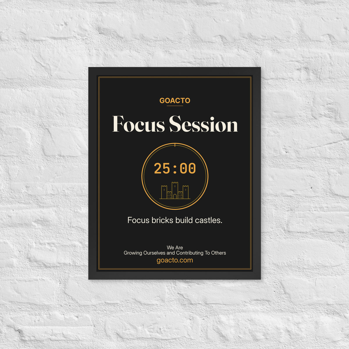Focus Session Framed Print, Brick Rise design, 16x20 in a black frame on a white brick wall: thin amber ring around a 25:00 timer with a small line-drawn castle inside, on charcoal, the line 'Focus bricks build castles.' and 'We Are / Growing Ourselves and Contributing To Others' above goacto.com