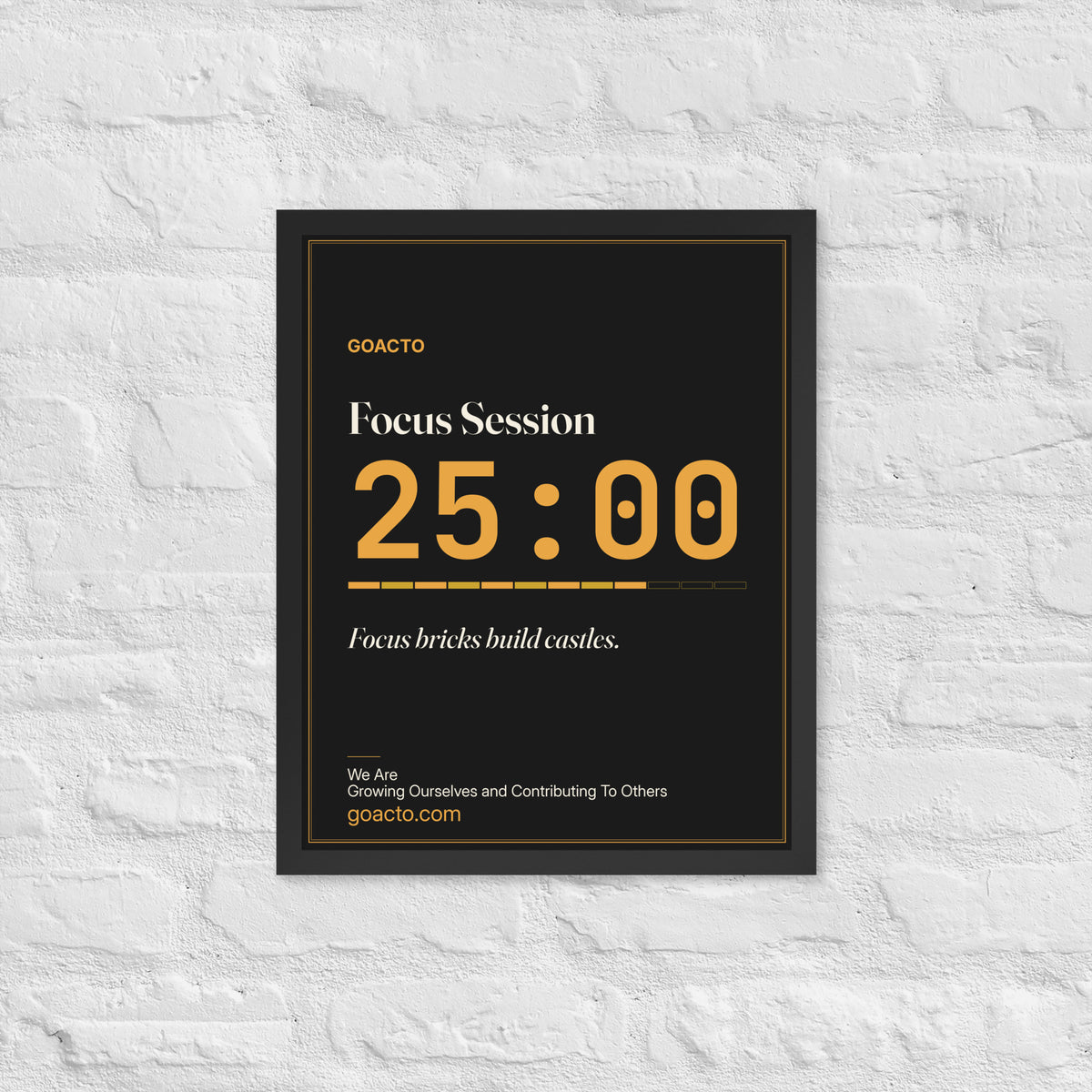 Focus Session Framed Print, Type design, 16x20 in a black frame on a white brick wall: oversized amber 25:00 above a segmented progress bar, on charcoal, the line 'Focus bricks build castles.' and 'We Are / Growing Ourselves and Contributing To Others' above goacto.com