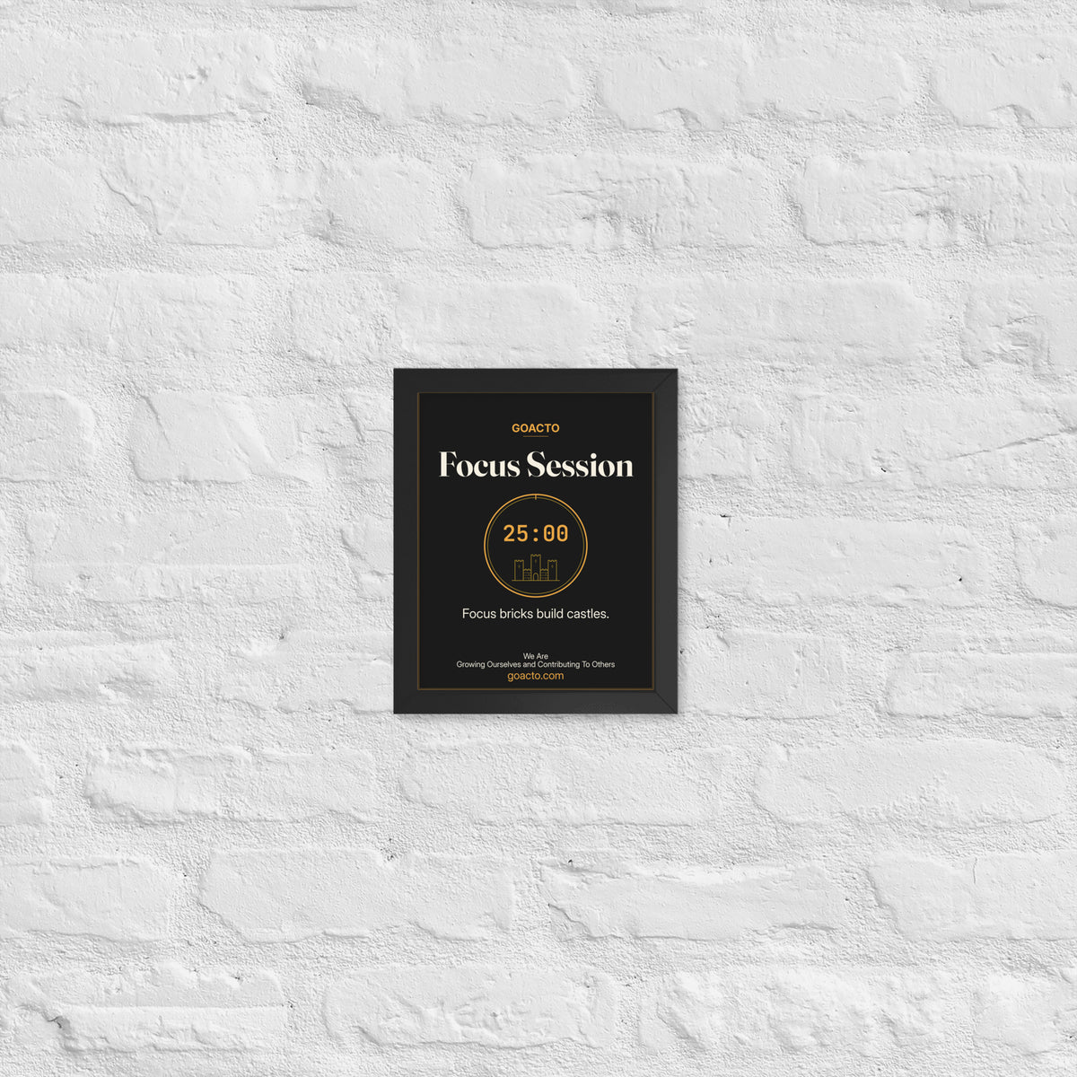 Focus Session Framed Print, Brick Rise design, 8x10 in a black frame on a white brick wall: thin amber ring around a 25:00 timer with a small line-drawn castle inside, on charcoal, the line 'Focus bricks build castles.' and 'We Are / Growing Ourselves and Contributing To Others' above goacto.com