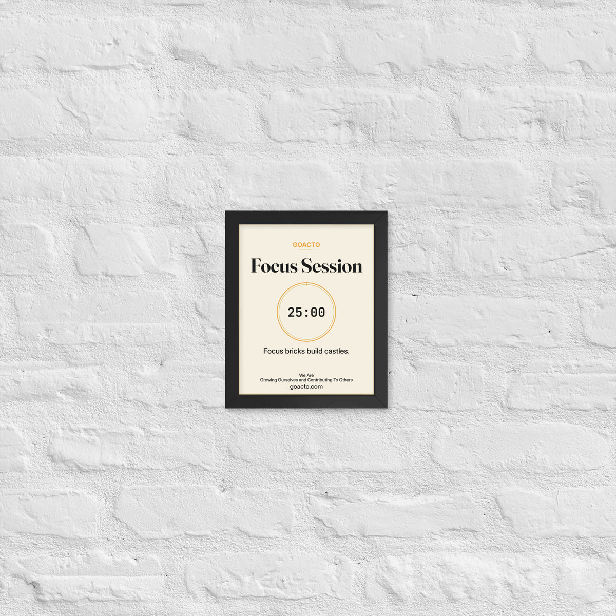 Focus Session Framed Print, Cream design, 8x10 in a black frame on a white brick wall: thin amber ring around a dark 25:00 timer, with dark type on a cream background, the line 'Focus bricks build castles.' and 'We Are / Growing Ourselves and Contributing To Others' above goacto.com