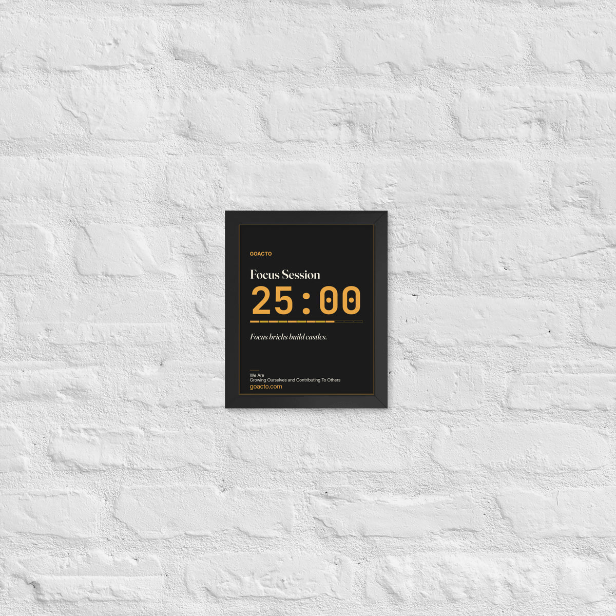 Focus Session Framed Print, Type design, 8x10 in a black frame on a white brick wall: oversized amber 25:00 above a segmented progress bar, on charcoal, the line 'Focus bricks build castles.' and 'We Are / Growing Ourselves and Contributing To Others' above goacto.com